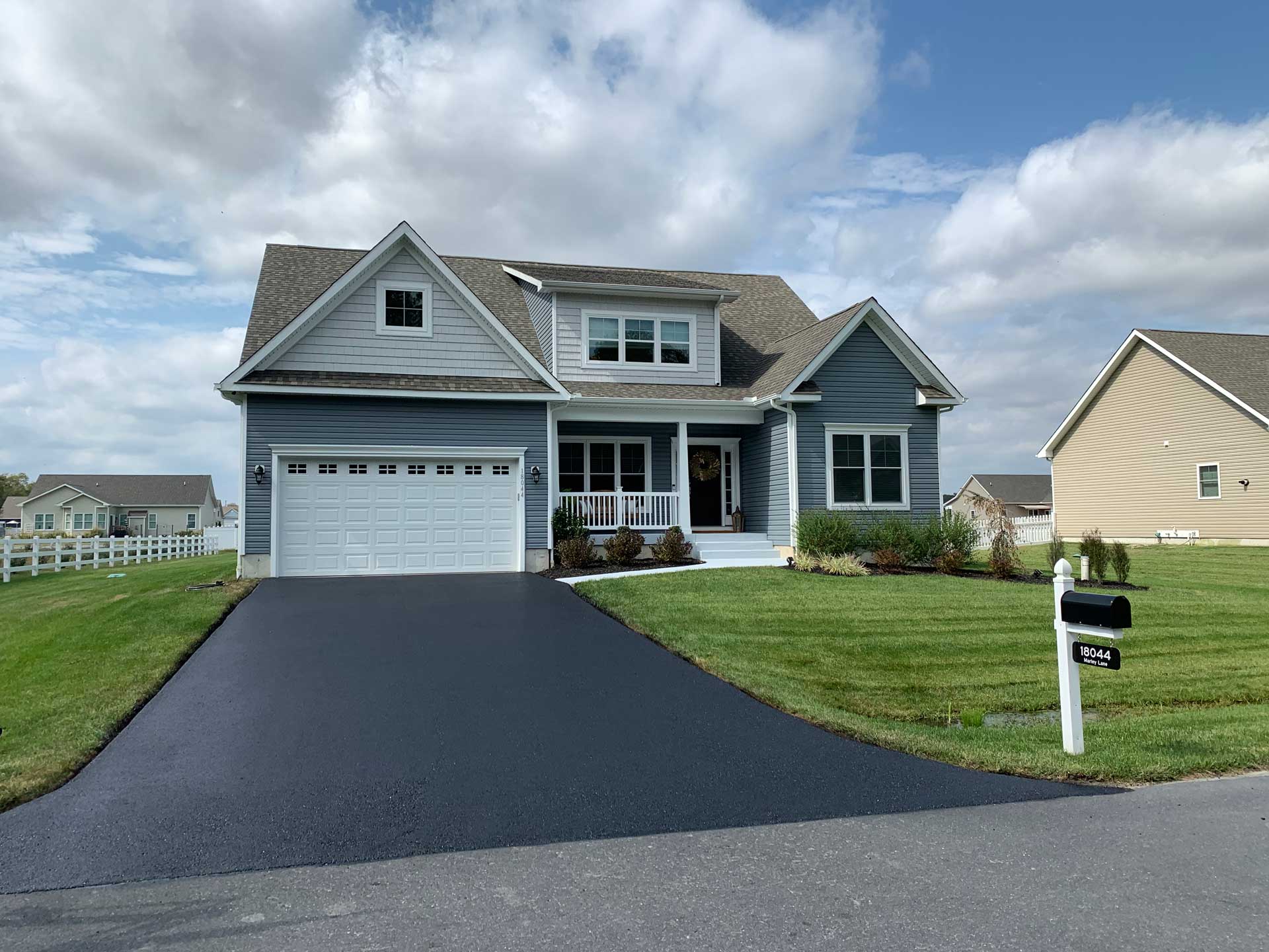 A blue house with a freshly-sealed driveway by JD Asphalt