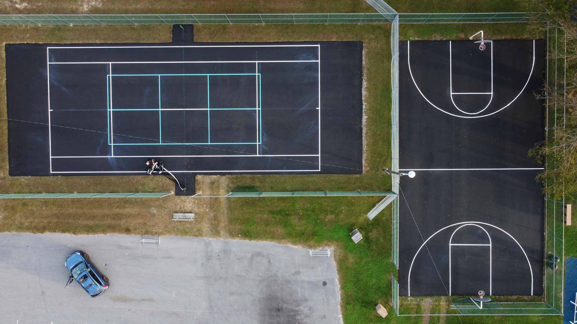 Overhead drone shot of a newly paved basketball court and tennis court. Both have been striped